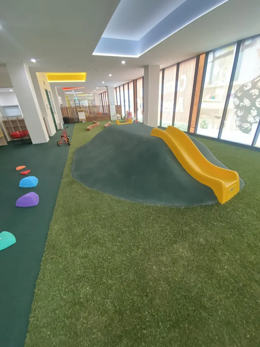 Indoor childcare play area with synthetic grass and a play mound